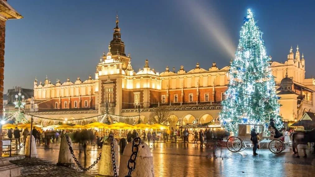 Christmas market at dusk in front of the Cloth Hall on Kraków's Main Square, with a tall Christmas tree covered in lights